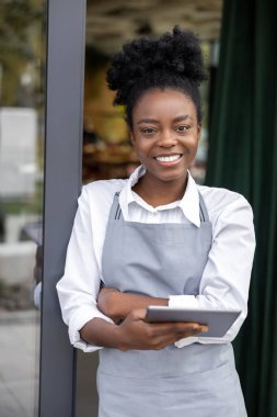 Kafe kapısında durup gülümseyen genç bir kadın