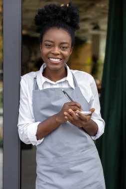 Elinde not defteriyle gülümseyen esmer tenli kız.