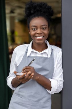 Elinde not defteriyle gülümseyen esmer tenli kız.
