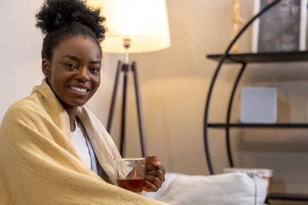 幸福的女人裹在温暖舒适的格子花里 端着一大杯茶坐在沙发上 — 图库照片