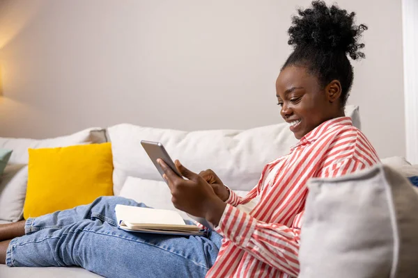 用数字平板电脑在线滚动网络应用来吸引乐观的女性在沙发上放松 — 图库照片