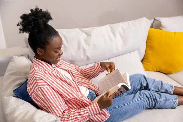 Sorridente Donna Afroamericana Leggere Libro Mentre Seduto Sul Divano Casa — Foto Stock