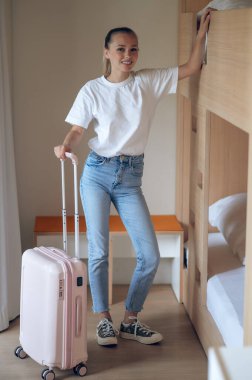 Beyaz gömlekli, kot pantolonlu, otel odasında gülümseyen güzel bir kadın..