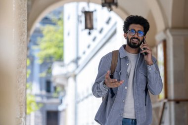 Telefondaki. Koyu renk saçlı adam kemerde yürüyor ve telefonla konuşuyor.