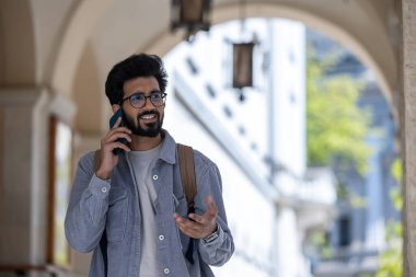 Telefondaki. Koyu renk saçlı adam kemerde yürüyor ve telefonla konuşuyor.