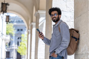 Turist. Elinde bir telefonla kemerde gülümseyen siyah saçlı adam.