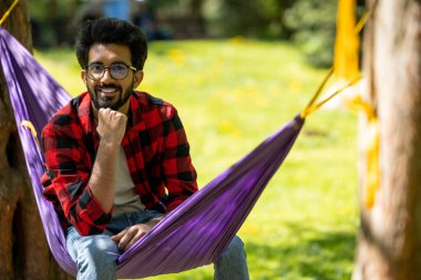 Genç Hintli adam parkta hamakta oturuyor.