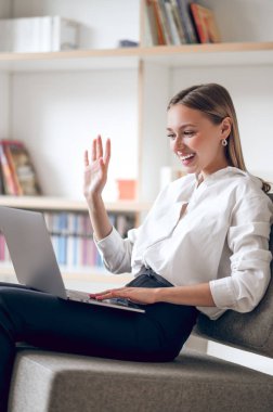 Güzel bir kadın dizüstü bilgisayarında oturup el sallarken selam veriyor..
