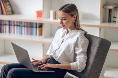 Oturma odasında otururken dizüstü bilgisayar kullanan neşeli beyaz kadın..