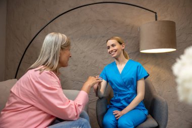 Hemşire, tıp merkezinde nabız oksimetresi kullanan yaşlı kadına oksijen doygunluğunu ölçüyor..