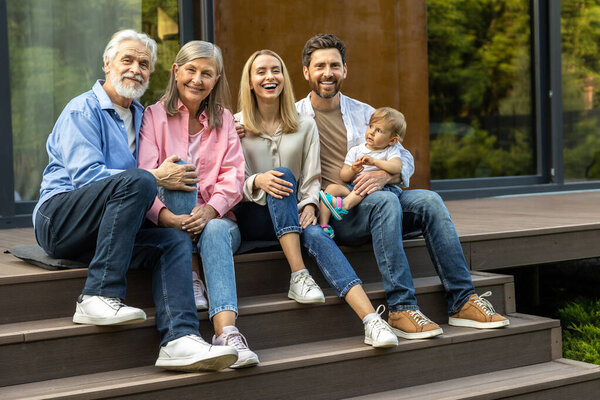 Счастливая большая семья сидит на ступеньках дома