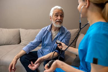 Sağlık merkezindeki kan basıncını ölçen olgun bir hastayı muayene eden hemşire..