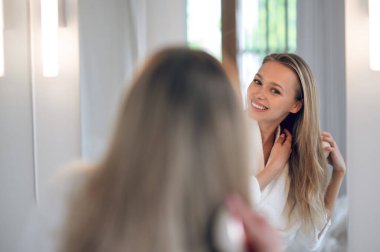 Saç yapıyorum. Uzun saçlı güzel kadın aynada saç yapıyor.