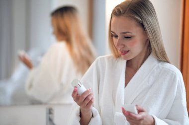 Yüz bakımı. Beyaz bornozlu kadın ellerinde yüz kremi tutuyor.