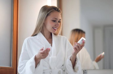 Yüz bakımı. Beyaz bornozlu kadın ellerinde yüz kremi tutuyor.