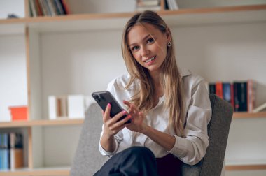 Sarışın kadın akıllı telefonunu internette gezinmek ya da sohbet etmek için kullanıyor..