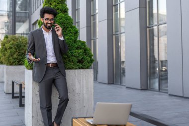 Koyu renk saçlı Hindu işadamı dışarıda çalışıyor ve telefonla konuşuyor.
