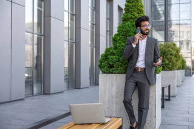 Koyu renk saçlı Hindu işadamı dışarıda çalışıyor ve telefonla konuşuyor.