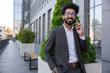 Koyu renk saçlı Hindu işadamı dışarıda çalışıyor ve telefonla konuşuyor.