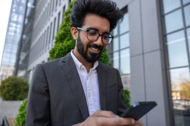 Sakallı, gülümseyen, yakışıklı Hindu işadamı. Elinde telefon var.