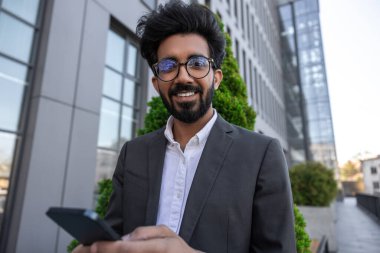 Sakallı, gülümseyen, yakışıklı Hindu işadamı. Elinde telefon var.