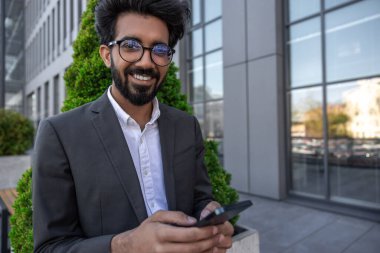 Sakallı, gülümseyen, yakışıklı Hindu işadamı. Elinde telefon var.