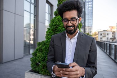 Sakallı, gülümseyen, yakışıklı Hindu işadamı. Elinde telefon var.