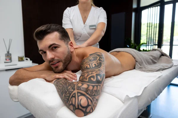 Back massage. Young man with a big tattoo having back massage session in a salon