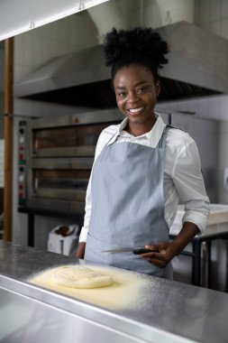 Afro-Amerikalı genç bir kadın pizzacı mutfağında pizza hazırlıyor.