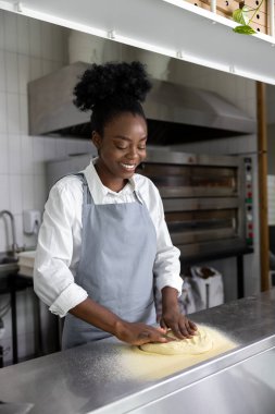 Afro-Amerikalı genç bir kadın pizzacı mutfağında pizza hazırlıyor.