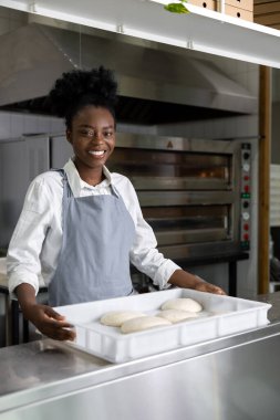 Afro-Amerikalı genç bir kadın mutfakta pizza hazırlıyor.