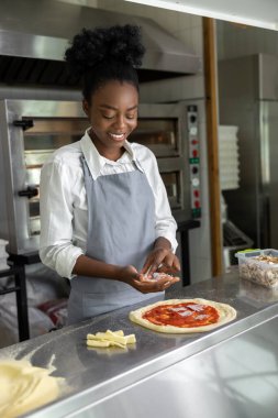 Afro-Amerikalı kadın pizza pişiriyor ve gülümsüyor.