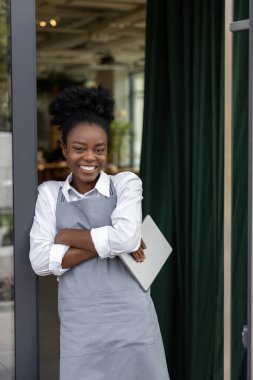 Kafe kapısında durup gülümseyen genç bir kadın