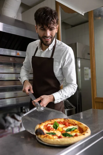Dark-haired young man cooking pizza in pizzeria