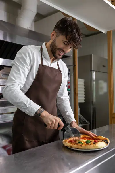 Dark-haired young man cooking pizza in pizzeria