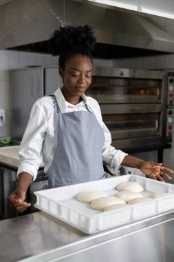 Afro-Amerikalı genç bir kadın pizzacıda pizza pişiriyor.