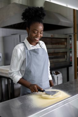 Afro-Amerikalı genç bir kadın pizzacı mutfağında pizza hazırlıyor.
