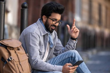 Düşünceli. Siyah saçlı genç adam düşünceli bir bakışla kaldırımda oturuyor.