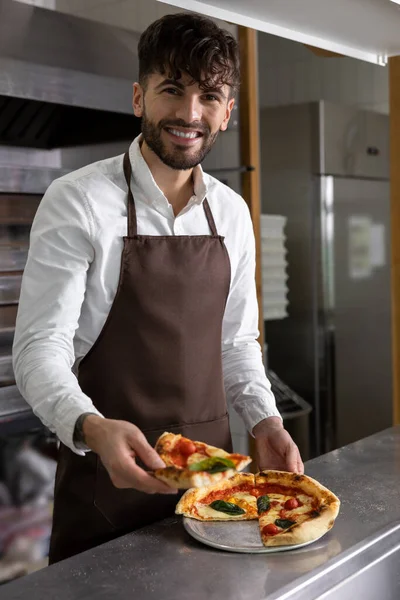 Smiling dark-haired pizzeria worker with pizza slice in hands