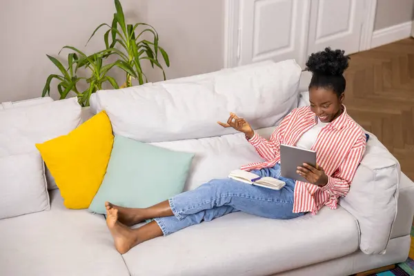 一个富有创造力的女人 坐在舒适的沙发上 一边在日记本上做笔记 一边在平板电脑上工作 — 图库照片