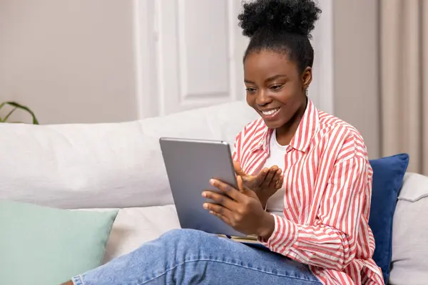 用数字平板电脑检查社交媒体在线交流的黑人女性坐在客厅的沙发上 — 图库照片