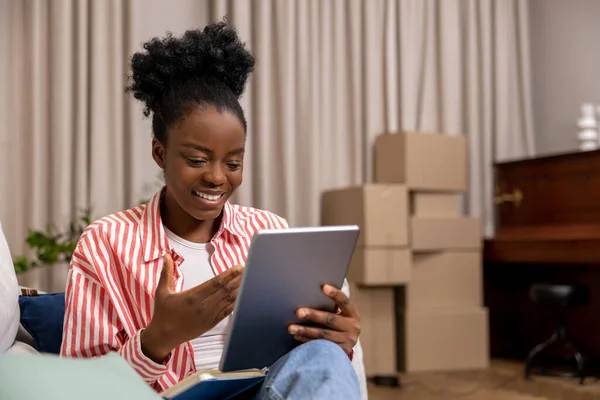 带着纸板箱搬新房子后 对非洲发型满意的女性在网上用平板电脑聊天 — 图库照片