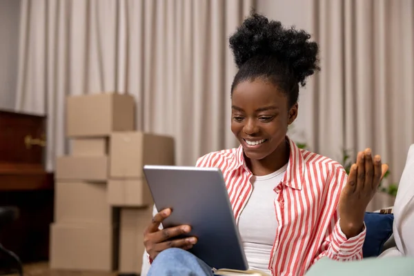 拥有非洲式发型的快乐女人坐在沙发上 通过数码平板电脑进行视频通话 — 图库照片