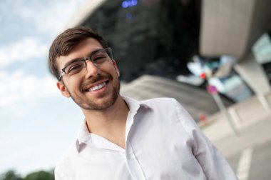 Keyfin yerinde. Koyu renk saçlı, beyaz gömlekli genç adam gülümsüyor.