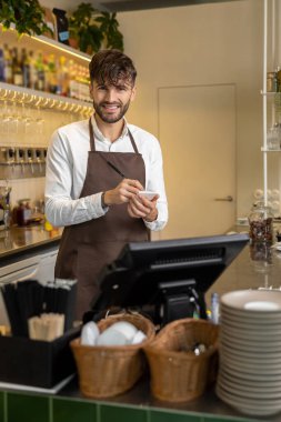 Pizzacının garsonu not alıyor ve gülümsüyor.