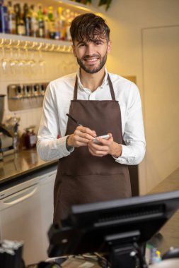 Pizzacının garsonu not alıyor ve gülümsüyor.