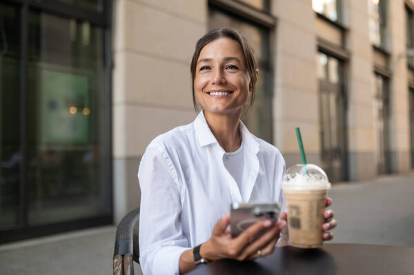 Dark-haired woman having coffee and holding a phone in hand