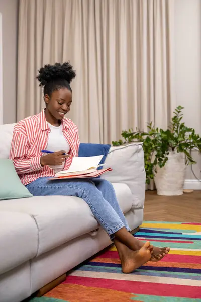 黑人妇女坐在家里的沙发上 一边写单子 一边计划着一天的工作 — 图库照片