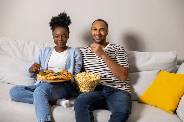 屋内ソファに座っているコメディ映画を見ながらピザとポップコーンを食べる楽しいカップル — ストック写真