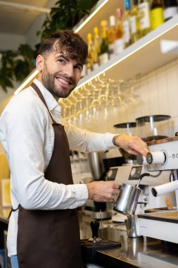 Kahve makinesinin yanında duran gülümseyen barista.